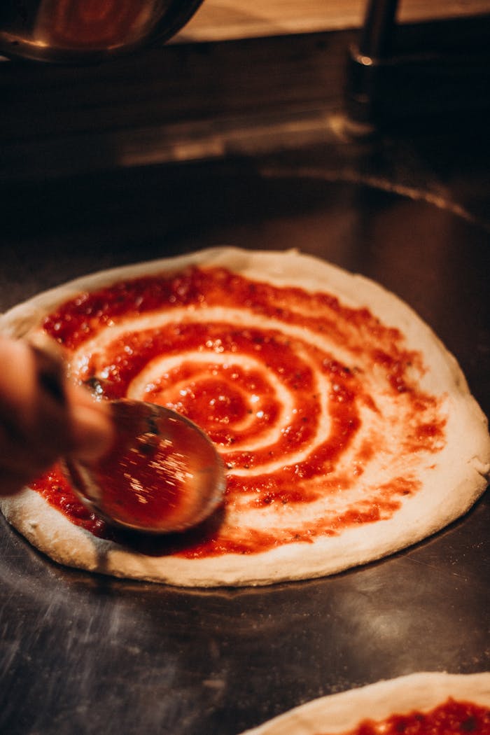 Close-up of a chef skillfully spreading tomato sauce on pizza dough.